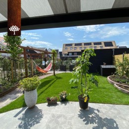 Voor deze tuin naar eigen ontwerp hebben we gekozen voor grote keramische tegels in combinatie met organische vormen. We plaatsen een hardhouten pergola tussen de beukenhaag en over het pad om meer dieptewerking te krijgen. <br />
<br />
De maatwerk doorloop schuur g